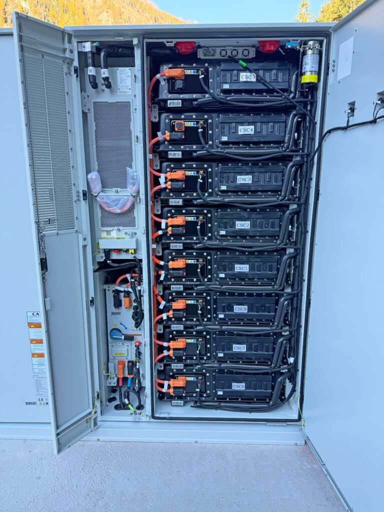 Geöffneter Batteriespeicher-Schaltschrank mit gestapelten Batteriemodulen, Verkabelung und Steuerungseinheit im Außenbereich.