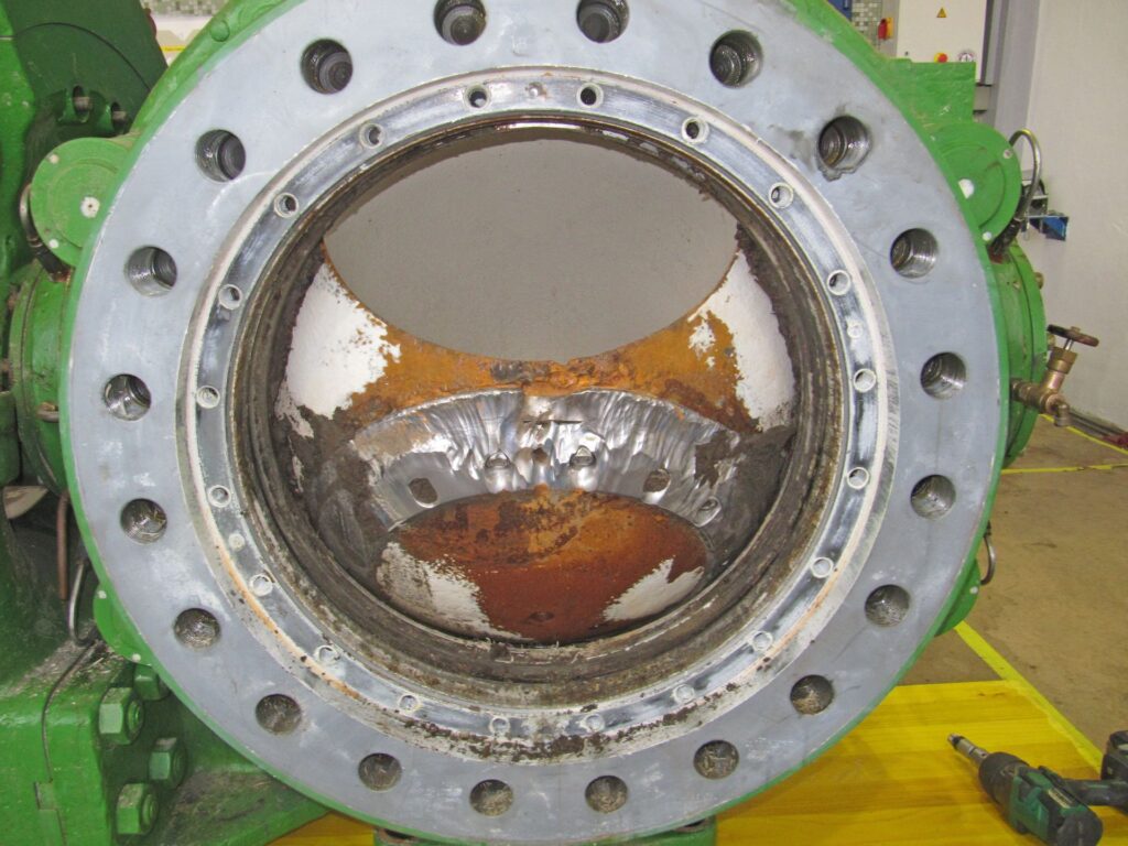 Geöffneter Flansch eines grünen Industrie-Kugelhahns mit starkem Rost und Materialverschleiß im Inneren.