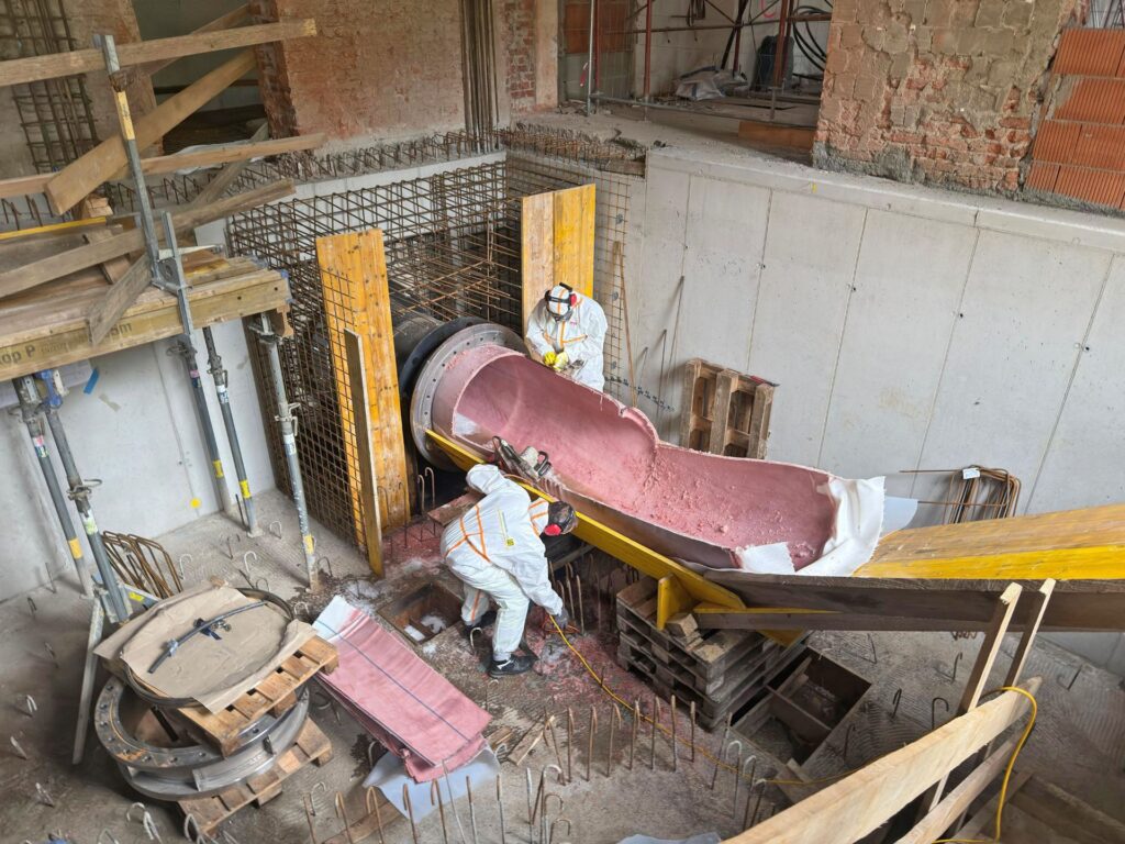 Zwei Arbeiter in Schutzkleidung bei der Inlinermontage zur Rohrsanierung auf einer Baustelle mit Bewehrungsstahl.