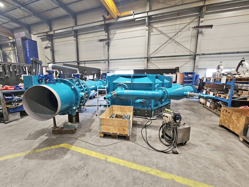 Blaues KW Mega Rema Gehäuse mit Verteilrohrleitung (122 x 90 mm) in einer Industrie-Fertigungshalle für Wassertechnik.