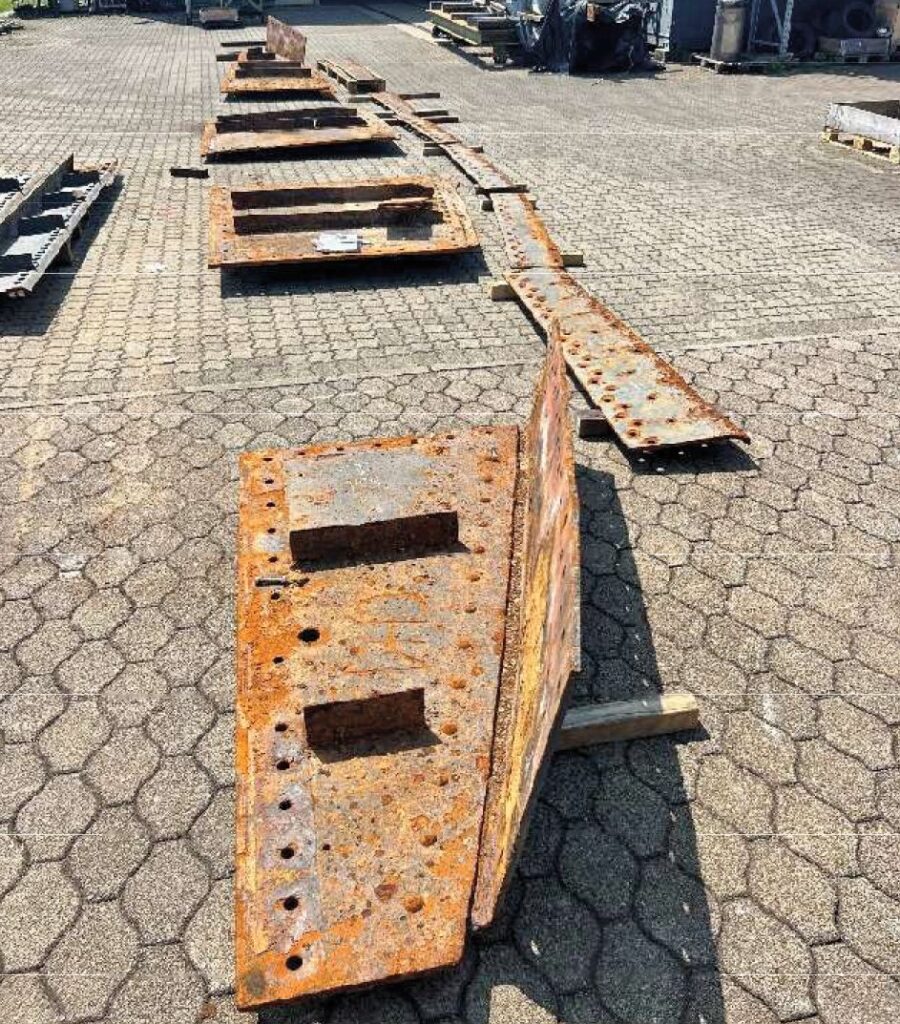 Rostige Lochbleche und schwere Stahlplatten auf einem gepflasterten Industriegelände im Außenbereich.