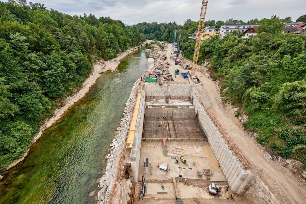Neubau des Kraftwerks Traunfall: Große Baustelle mit Kran und Betonfundamenten direkt am Flussufer der Traun im Wald.