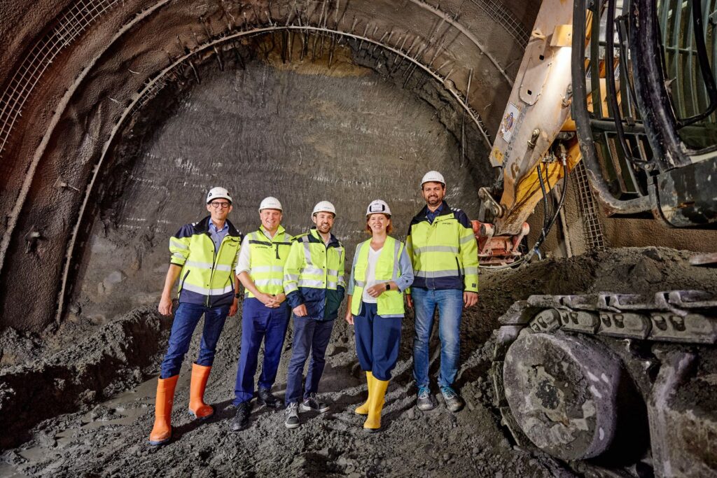 Lokalaugenschein beim Neubau des Kraftwerks Traunfall: Fünf Personen in Warnwesten im Tunnelvortrieb neben einem Bagger.