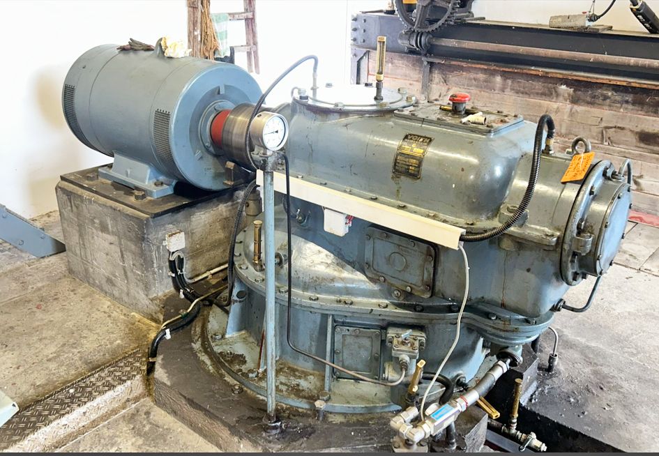 Alte industrielle Voith-Maschine aus hellblauem Metall mit Manometer und Motor in einer Werkshalle auf Betonsockel.