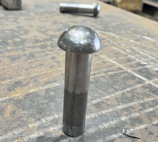 Aufrecht stehende metallische Vollniete mit rundem Kopf auf einer abgenutzten Werkbank in einer Werkstatt.