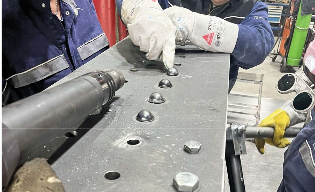 Industrieller Nietprozess an einer Stahlplatte mit mehreren gesetzten Halbrundnieten und Arbeiter in Schutzkleidung.
