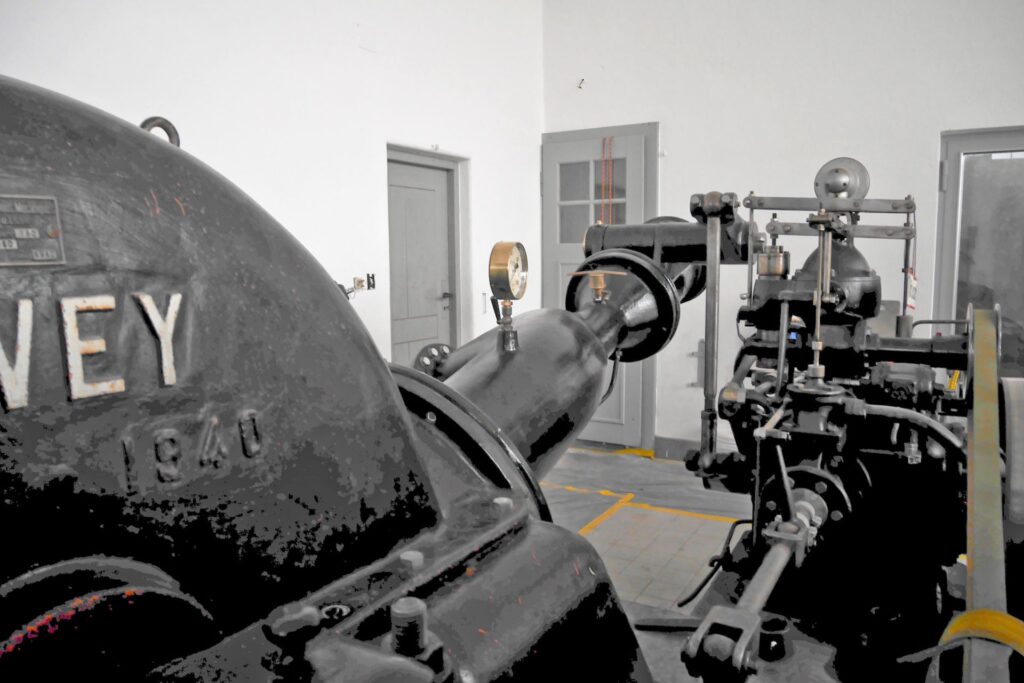 Schwarze Wasserturbine von 1940 mit Manometer und mechanischen Bauteilen in einer historischen Industriehalle.