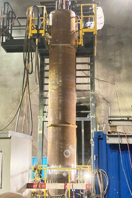 Vertikale Rohrschweißmaschine an einem Stahlrohr in einer Tunnelbaustelle mit gelben Sicherheitsgeländern.