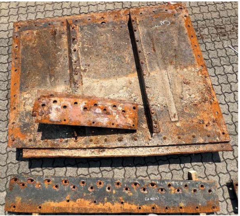 Verrostete Strömungsbleche aus Metall mit Bohrlöchern und Verstrebungen auf grauem Pflastersteinboden.