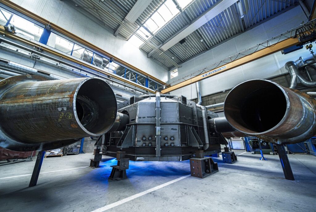 Große Turbine der Troyer AG in einer Industriehalle mit Stahlrohren und Deckenkran zur Montage von Wasserkraftanlagen.