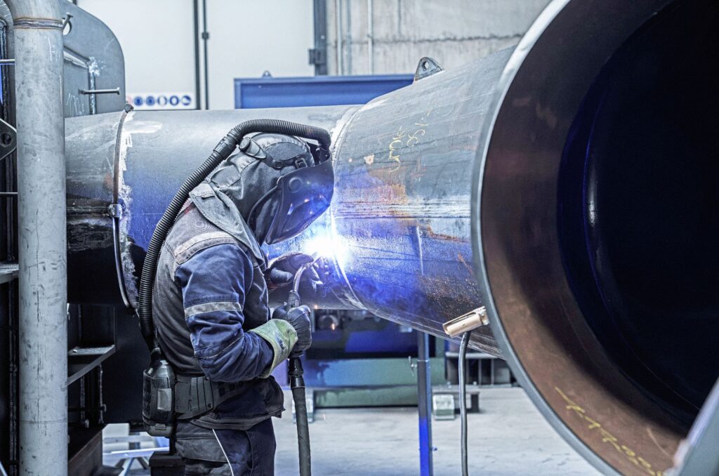 Schweißer der Troyer AG bei Arbeiten an einer großen Turbine mit Schutzausrüstung und hellem Lichtbogen in der Werkstatt.