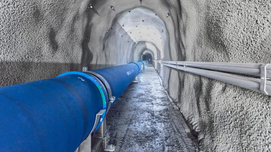 Blaue Druckleitung aus Guss im beleuchteten Sousbach-Stollen des Wasserkraftwerks.