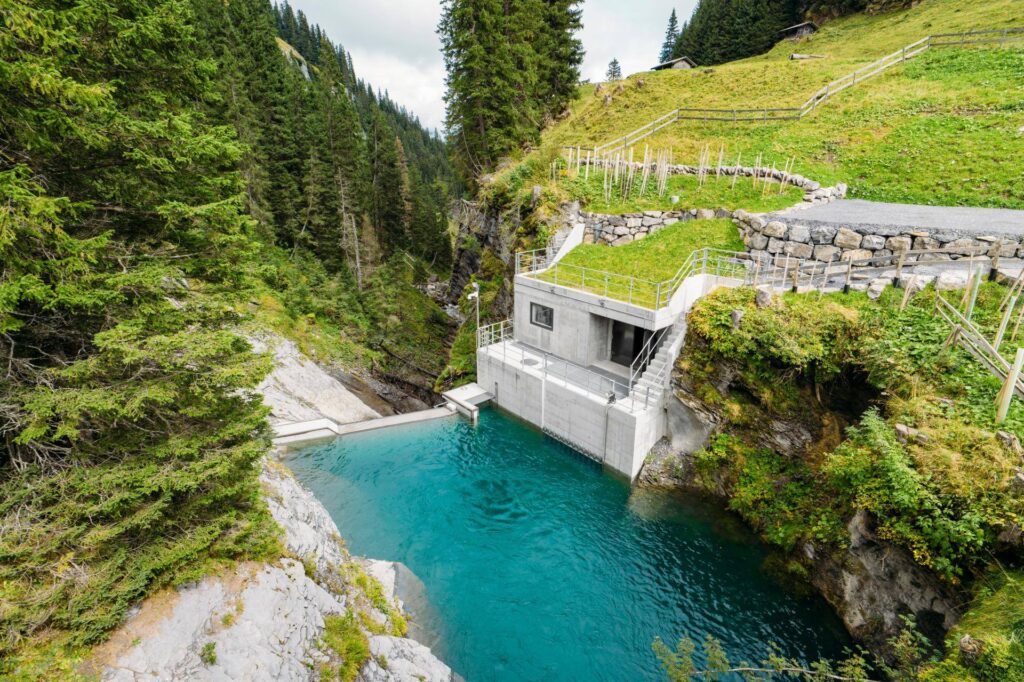 Wasserfassung des Wasserkraftwerks Sousbach in einer Waldschlucht mit türkisfarbenem Staubecken und Betonanlage.