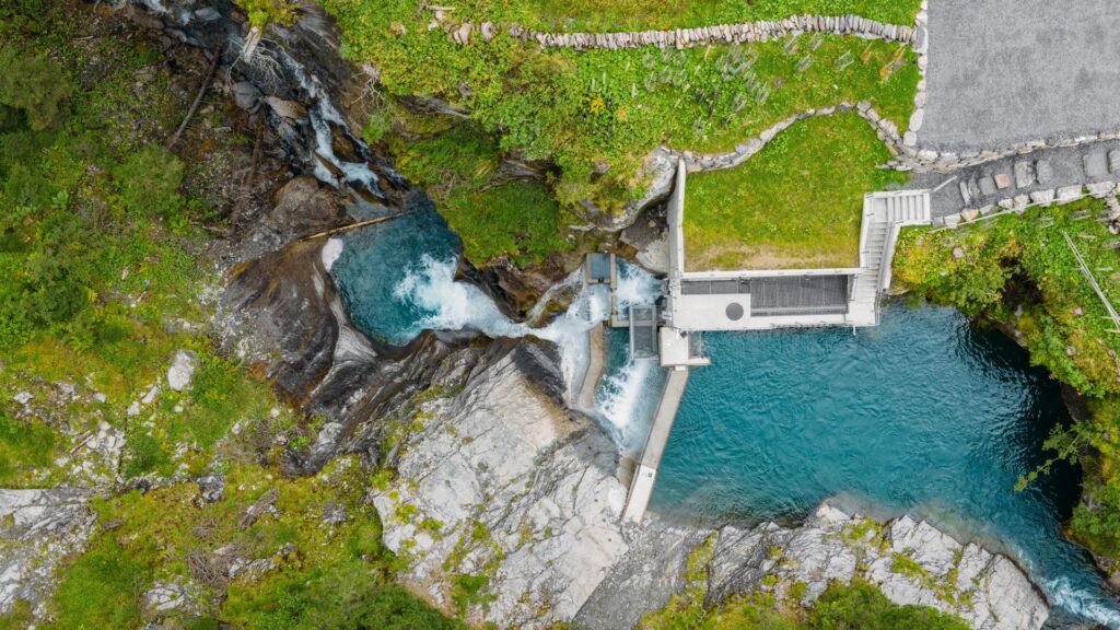Draufsicht auf die Wasserfassung am Sousbach: Türkisfarbenes Gebirgswasser fließt durch Felsen und Betonstrukturen des WKW.