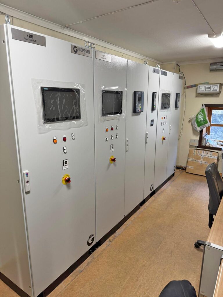 Graue Industrieschaltschränke von Geppert Electric mit Displays, Bedienelementen und Not-Aus-Schaltern in einem Kontrollraum.