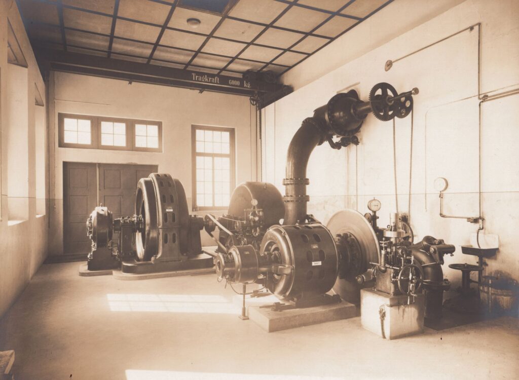 Historische Zentrale 2 mit industriellen Generatoren, großen Rohrleitungen und Deckenkran in einer Fabrikhalle.