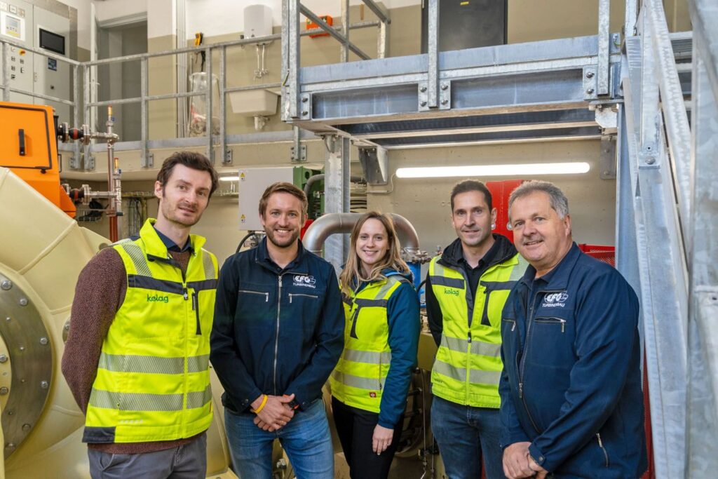 Gruppenfoto vom Kelag-Team im Kraftwerk Hüttenberg vor technischer Anlage in Arbeitskleidung und Warnwesten.